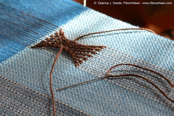 Blue fabric on the loom with warp sprang hourglass motif in brown